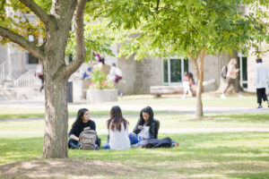 three female students sitting by a tree