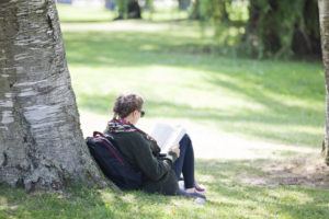 female student reading by tree outside